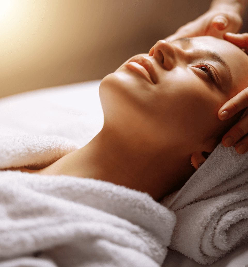 An esthetician gently touches a woman's scalp during a facial skin care service.